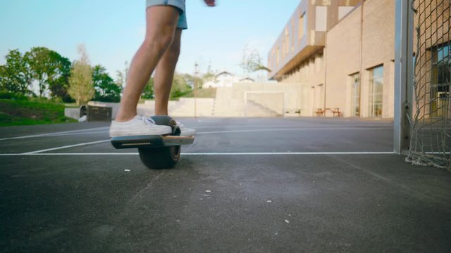 Young mand boarding One Wheel skating away in schoolyard with threes and blue sky during summer shot from frogs eye perspective