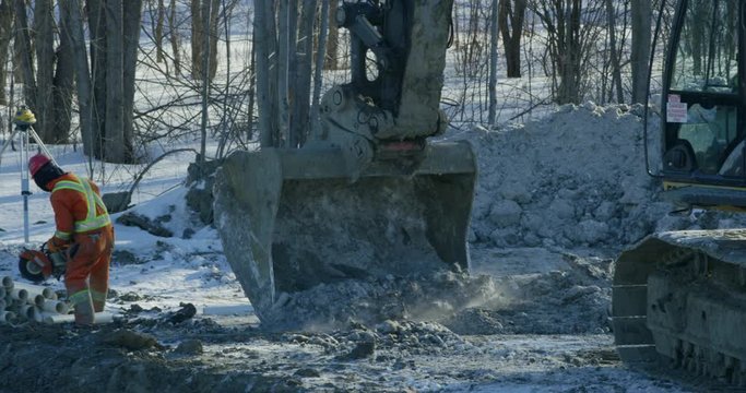 Construction site in winter - excavtor working next to workers - slow motion