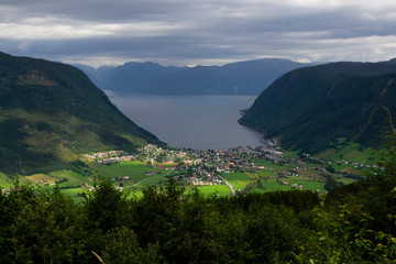 Fototapeta na wymiar View of the village of Vikøyri on the southern shore of the Sognefjorden, Vik commune in Norway on a cloudy day. The sun light struggle through clouds illuminating the village. Travel destination.