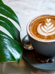 Cup of coffee on marble table with tropical monstera leaf