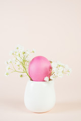 Easter painted pink egg in a stand on a pastel beige background with copy space.