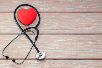 A heart with a stethoscope lies on a light wooden background. Healthy heart