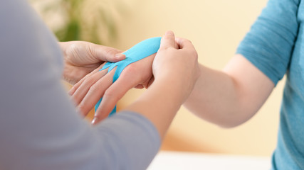 Female physiotherapist applying kinesio tape on patient's arm. Kinesiology, physical therapy, rehabilitation concept. Cropped shot.