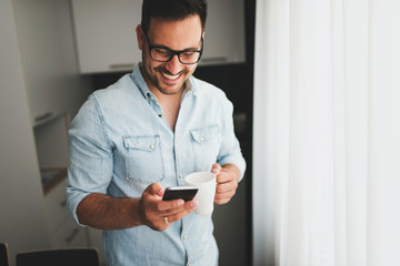 Happy handsome man drinking coffee in the morning texting on smartphone.