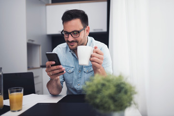 Happy handsome man drinking coffee in the morning texting on smartphone.