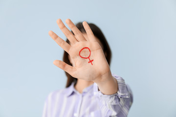 Woman with drawn symbol of woman on her palm against color background. Concept of feminism
