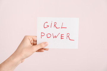 Female hand holding paper sheet with text GIRL POWER on color background. Concept of feminism