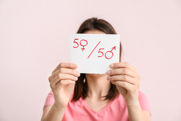 Woman holding paper sheet with simple fraction and symbols of woman and man on color background....