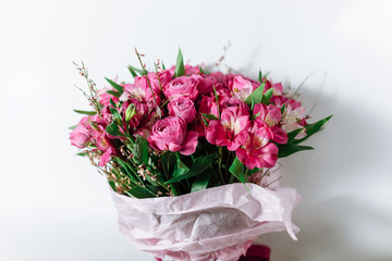 Flower bouquet of pink roses and other mixed flowers wrapped in soft pink paper. White background