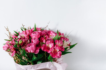 Flower bouquet of pink roses and other mixed flowers wrapped in soft pink paper. Copy space. White background