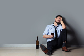 Businessman drinking wine near grey wall. Concept of alcoholism