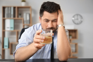 Drunk businessman with glass of whiskey in office. Concept of alcoholism