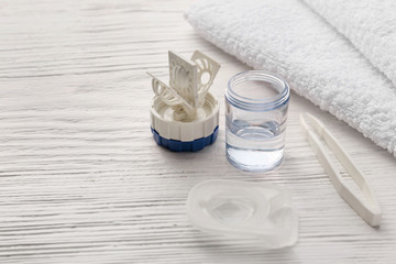 Container for contact lenses, tweezers and towel on white wooden background