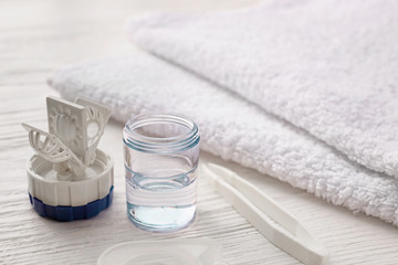 Container for contact lenses, tweezers and towel on white wooden background