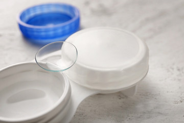 Container with contact lenses on light background, closeup