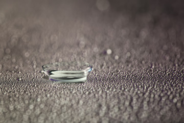 Contact lens and water drops on grey background