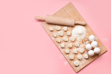 Raw fresh dumplings with rolling pin and eggs on color background