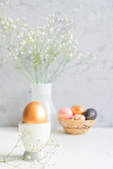 Obraz na płótnie Canvas Close up of Golden egg in egg cup on the background of bouquet of gypsophila. Cozy easter still life