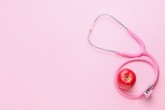 Fresh apple and stethoscope on color background