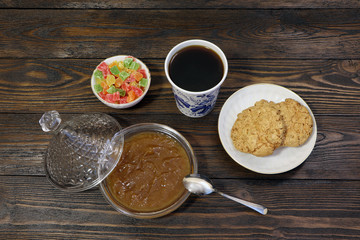 Breakfast. A cup of coffee, cookies, candied fruits and jam on a wooden table.