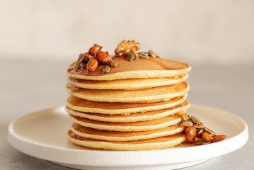 Stack of delicious pancakes with chocolate, honey, nuts and slices of banana on plate and napkin on wooden background