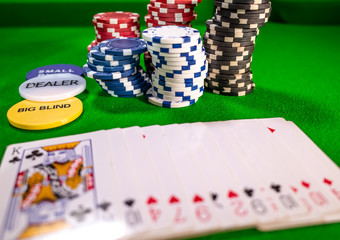 Close up of playing cards, poker chips and buttons on a green baize with selective focus on the stack of poker chips