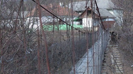 Fototapeta premium old pedestrian suspension bridge over a mountain river of metal bars and wooden floor