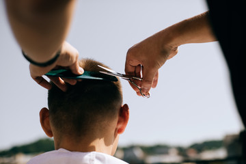 Hairdresser doing hairstyle with scissors to man outdoors, barber working