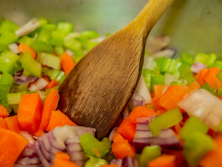 Selective focus on a wooden spoon in a saucepan full of freshly chopped vegetables when making a homemade soup dinner