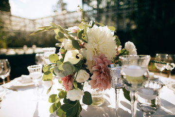 Catering servise. Beautiful table decor for a romantic dinner outdoors. Bouquets of flowers, candles, glasses on the table