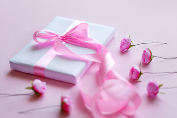 Composition of a white box and small pink flowers on a light pink background. Packing of gifts