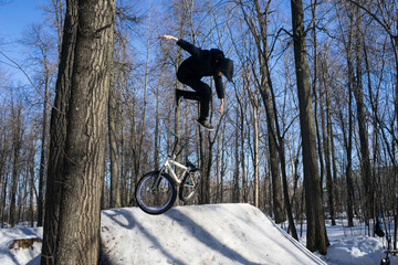 A cyclist does a 360 trick on a springboard in winter. Bmx rider shows a trick on a bicycle.