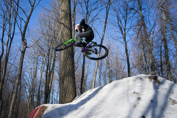 A cyclist does a 360 trick on a springboard in winter. Athlete shows a trick on a bicycle.