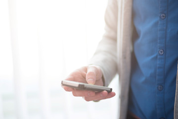 Man using his smartphone near the window. Close-up hand.