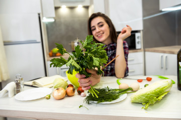 Girl posing at a kitchen table while prepares a salad of different vegetables and greens for a...