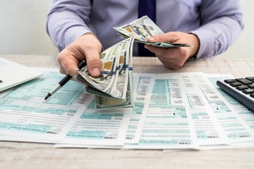 A businessman fills out an individual 1040 tax form and counts dollars. Male hands writing on paper...