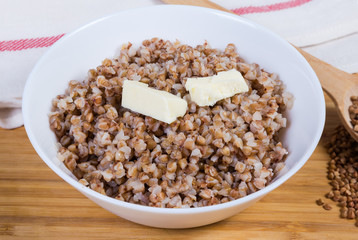 Buckwheat porridge with butter pieces in white bowl close-up