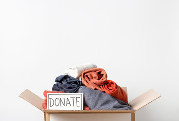 Clothes in cardboard box and the inscription Donate on a white background, front view, copy space