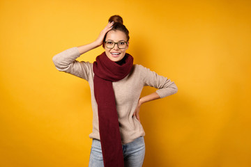 A beautiful brunette with a bunch on head and glasses stands in a sweater and a burgundy scarf,...