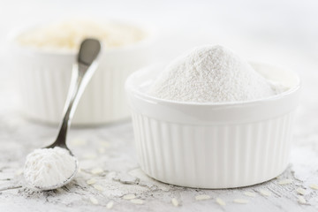 Rice flour in a bowl and spoon on a gray table. Gluten free, healthy diet concept.