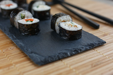 Sushi rolls with salmon, tuna, avocado, rice in algae and chopsticks on a dark board lying on a bamboo mat.