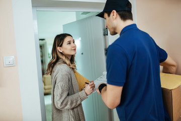 Young woman talking to a courier while signing for package delivery.