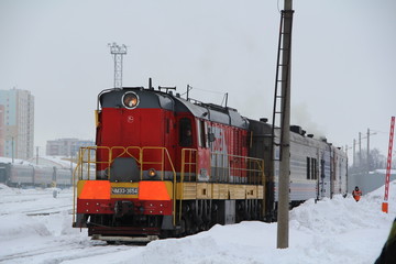 Red and white train locomotive at a railway station in winter against the backdrop of snow in Russia