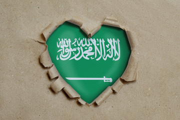 Heart shaped hole torn through paper, showing Saudi Arabia flag
