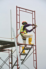 Construction workers wearing safety harness and installing scaffolding at high level in the...
