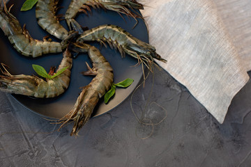 Fresh raw shrimp prawns on a black plate on a gray concrete background. Healthy seafood is a source of protein. Flat lay. Copy space.