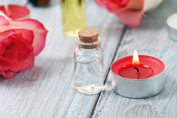 Obraz na płótnie Canvas Pink roses, oil bottles and burning candles on a gray wooden table. March 8. Valentine's Day. Greeting card. Romantic and beautiful background. Spa treatments. Personal care. Love and beauty.