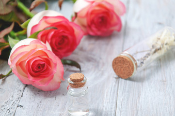 Obraz na płótnie Canvas Pink roses, oil bottles and candles on a gray wooden table. March 8. Valentine's Day. Greeting card. Romantic and beautiful background. Spa treatments. Personal care. Love and beauty.