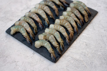Fresh raw peeled shrimp on a stone board on a gray concrete background. Healthy seafood is a source of protein. Flat lay.