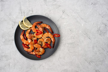 Tasty cooked fried shrimp with chilli and lemon on a gray concrete background. Healthy seafood. Copy space. Flat lay.